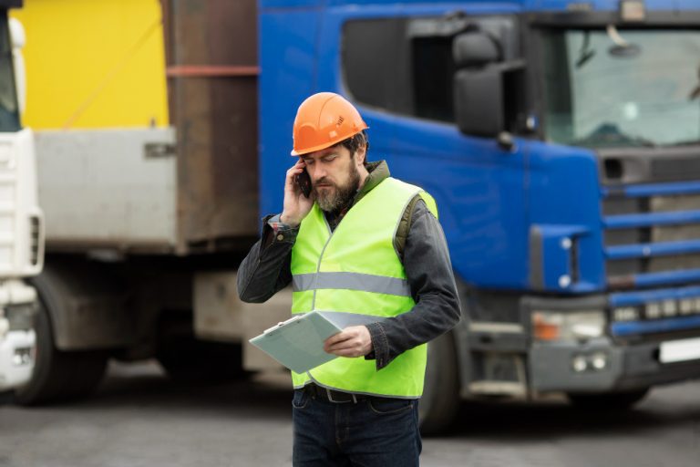Seguro em transportes 10 Motorista com documentos à mão em frente a caminhão parado ao fundo, ilustrando o impacto financeiro de uma paralisação
